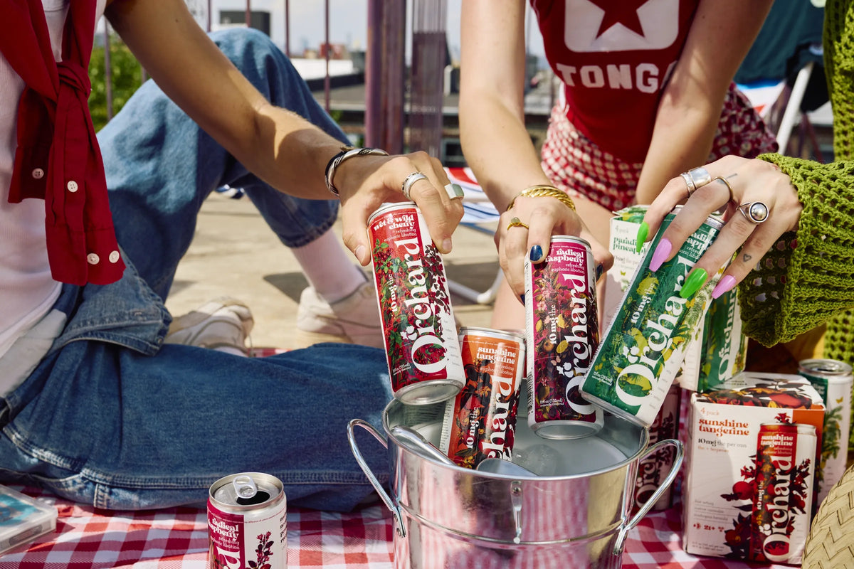 hands pulling Orchard cans from an ice bucket next to 4-pack boxes