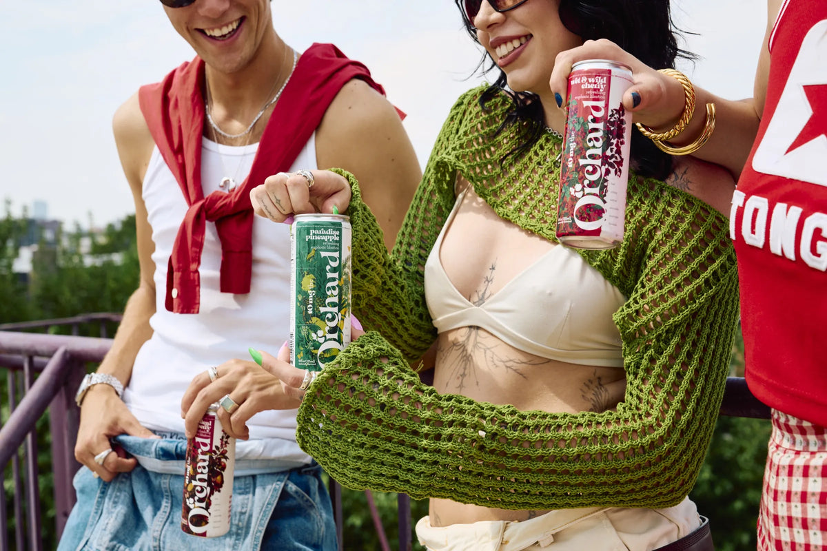 three friends holding Orchard cans on a rooftop