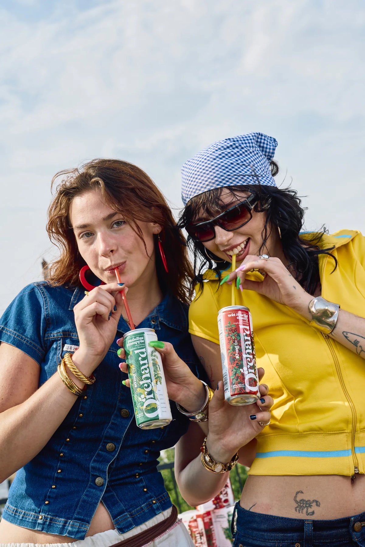 two friends sipping Orchard cans through straws on a rooftop