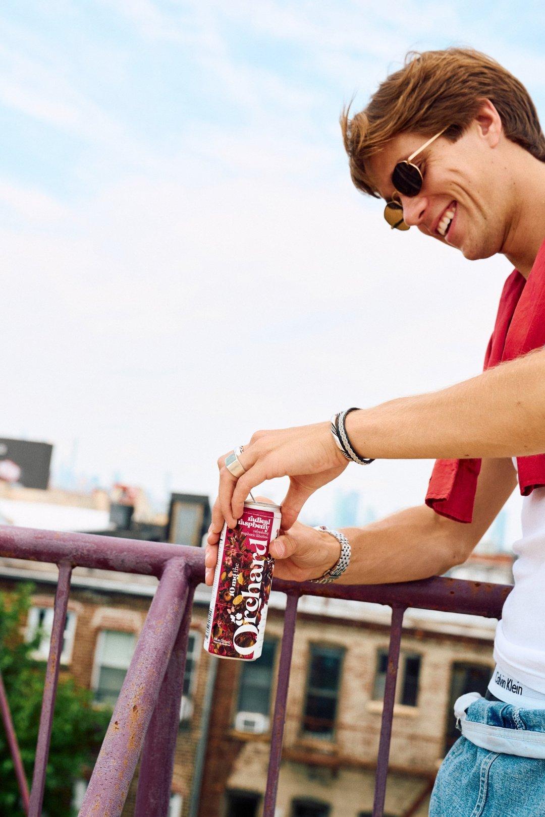 guy on a rooftop opening a can of Orchard